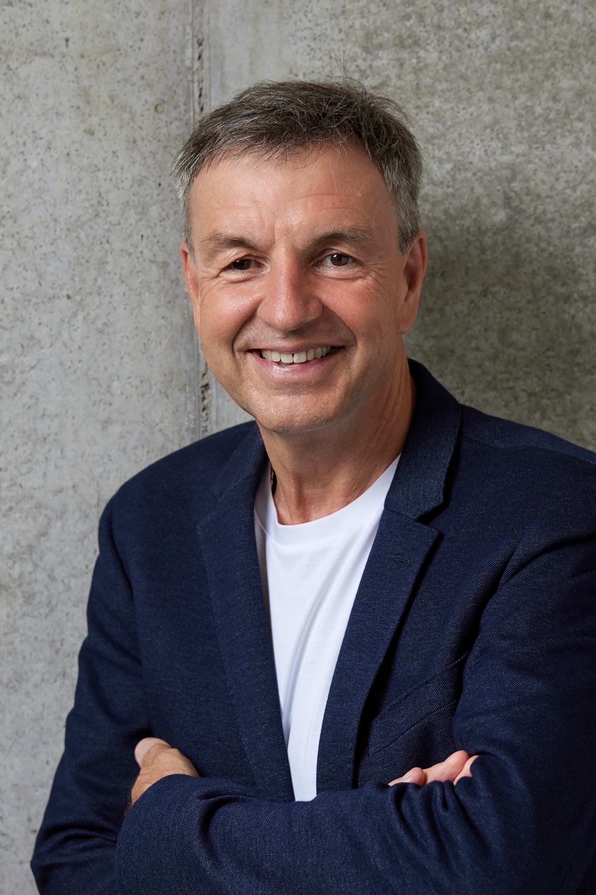 Michael Basler, Coach und Trainer, lächelnd mit verschränkten Armen vor einer Sichtbetonwand
