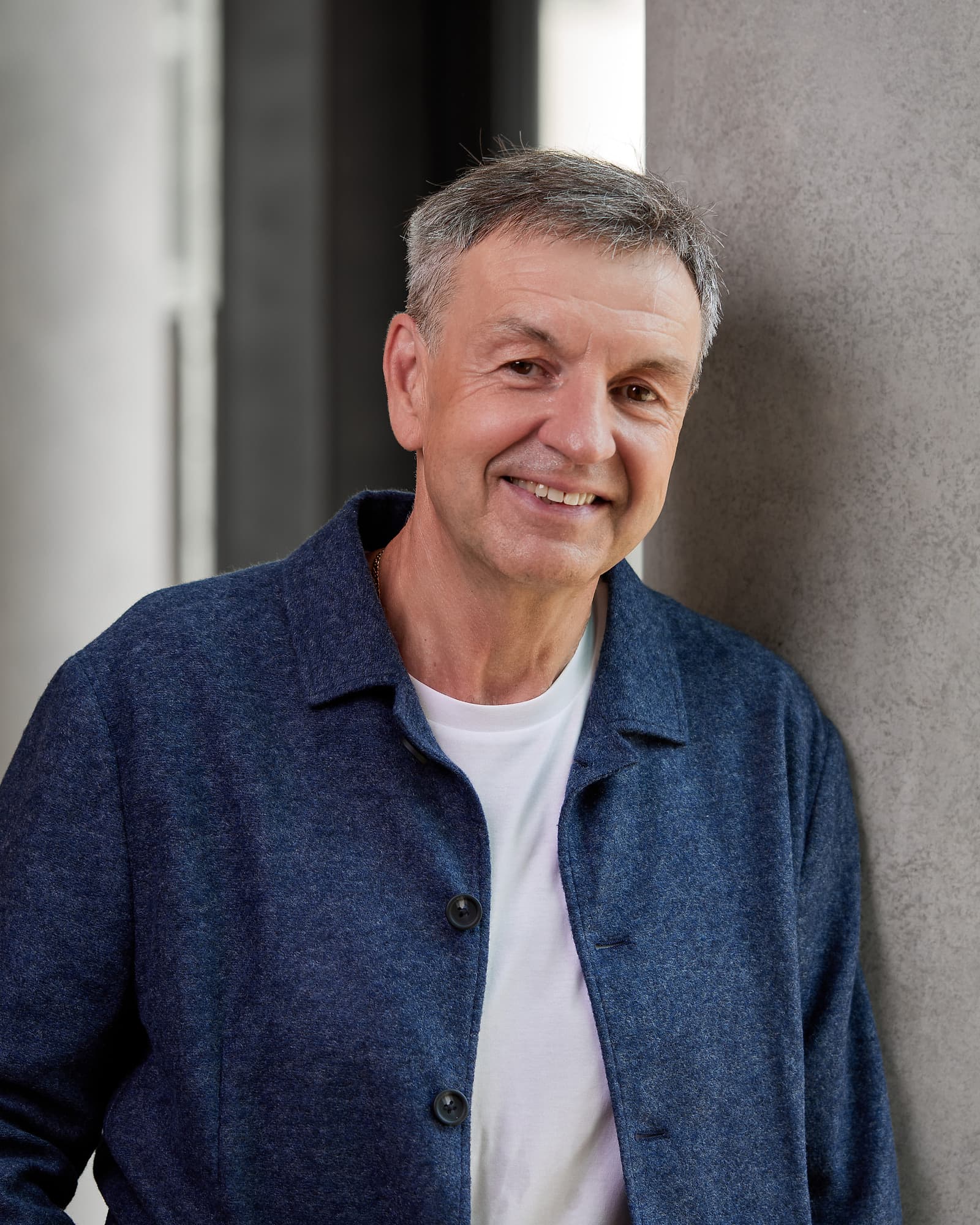 Michael Basler in blauer Jacke, entspannt an einen Betonpfeiler gelehnt